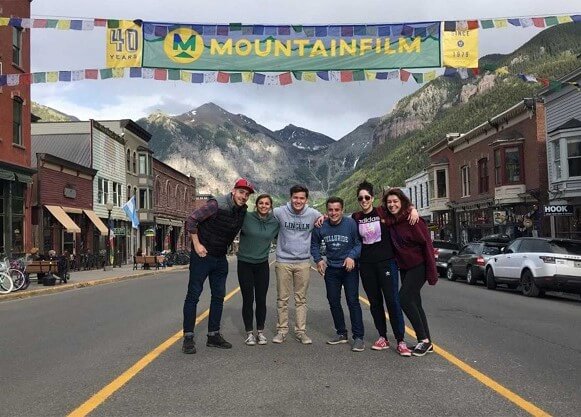 Students stand in street under banner with mountains in background