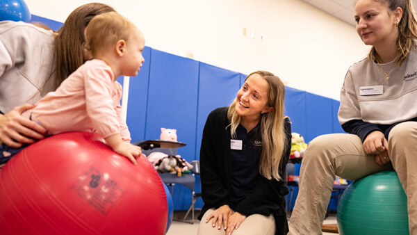 2 OT students speaking to a baby on a yoga ball