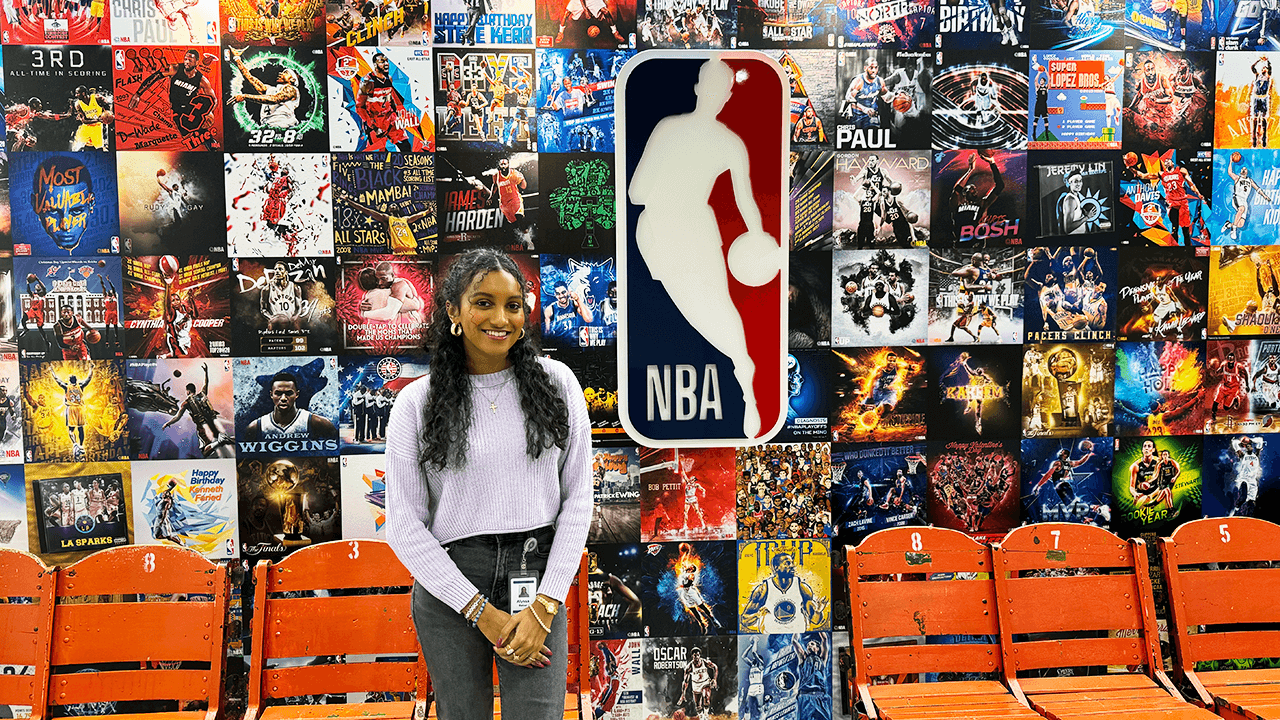 Grad Alyssa Baker smiles in front of the NBA sign.