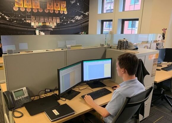 A male student sits at his desk in front of dual monitors working on spreadsheets