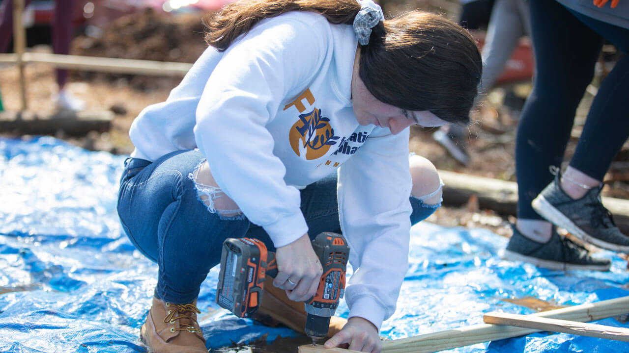 Girl drills into wood while helping build at the Big Event