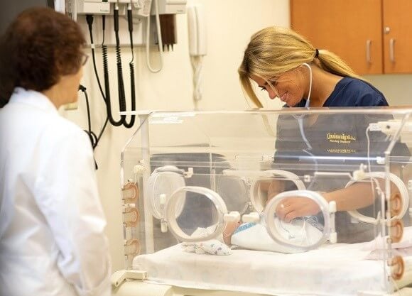 Ford examines a baby in an incubator with a nurse looking on