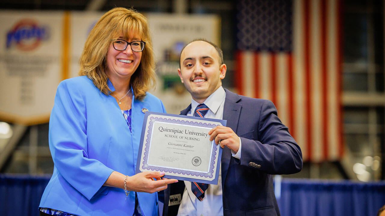 male student in a navy suit poses with dean lisa o'connor and the certificate he's being presented with