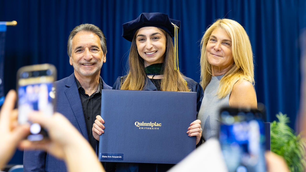 A graduate and her family pose for a photo as she holds her diploma