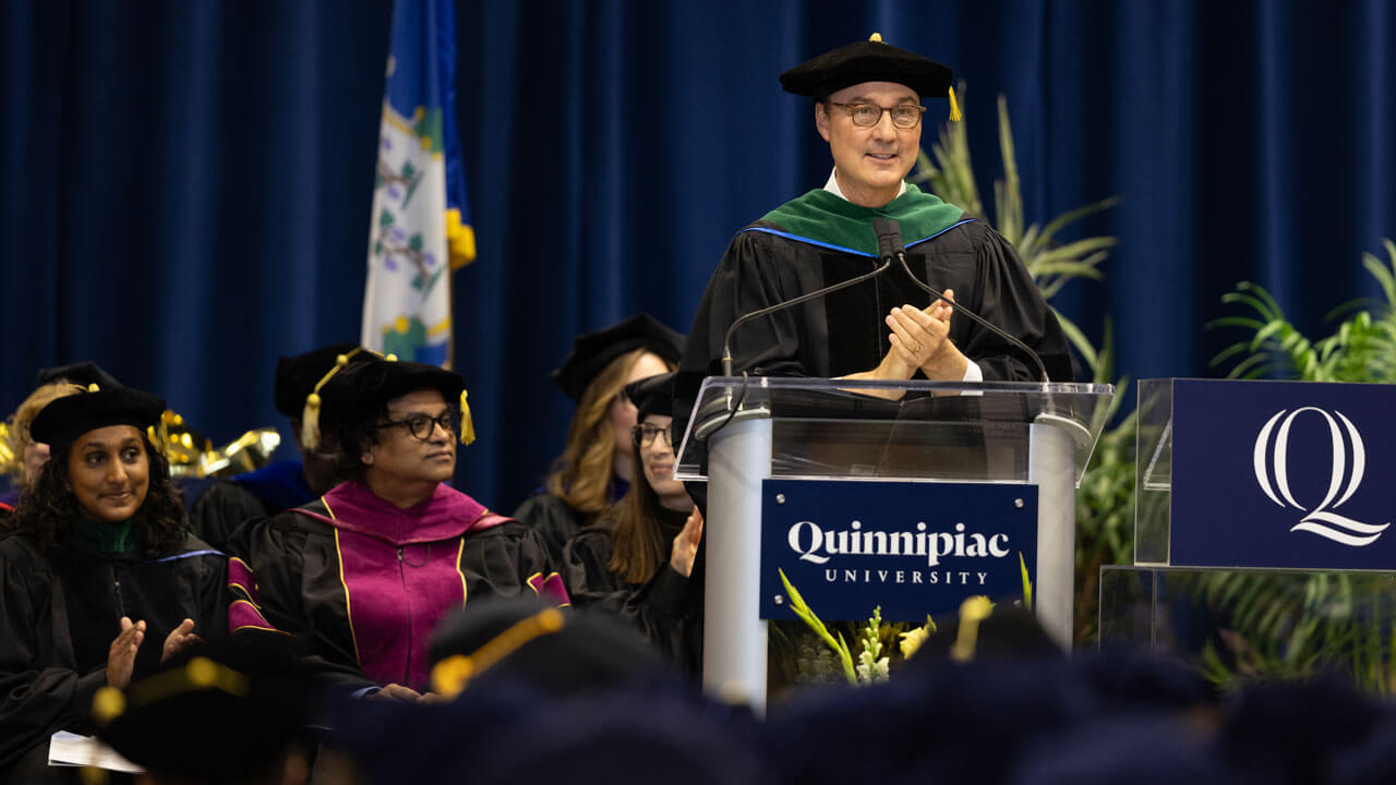 Dean Boiselle speaks at a podium on stage with faculty seated behind him