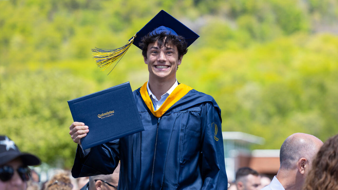Student walks through crowd smiling holding a diploma