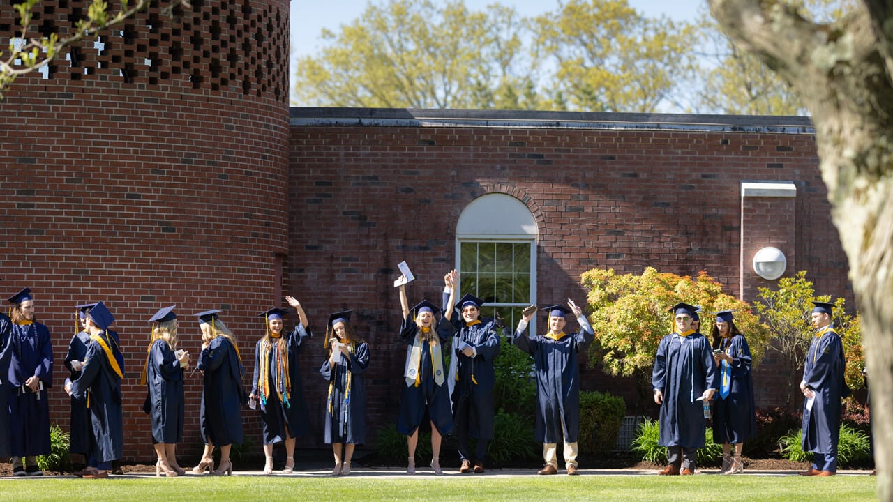 Dozens of graduates cheer and wave their arms as they wait in line