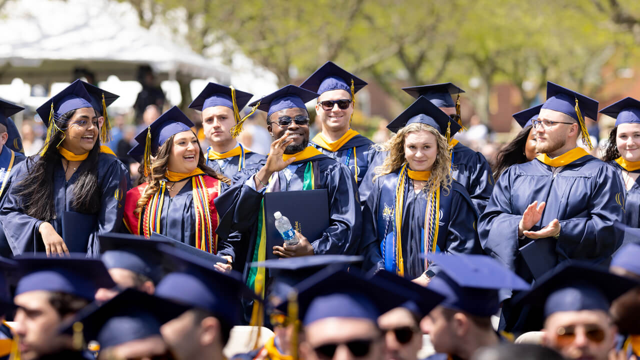 Several graduates stand and wave in front of their seats