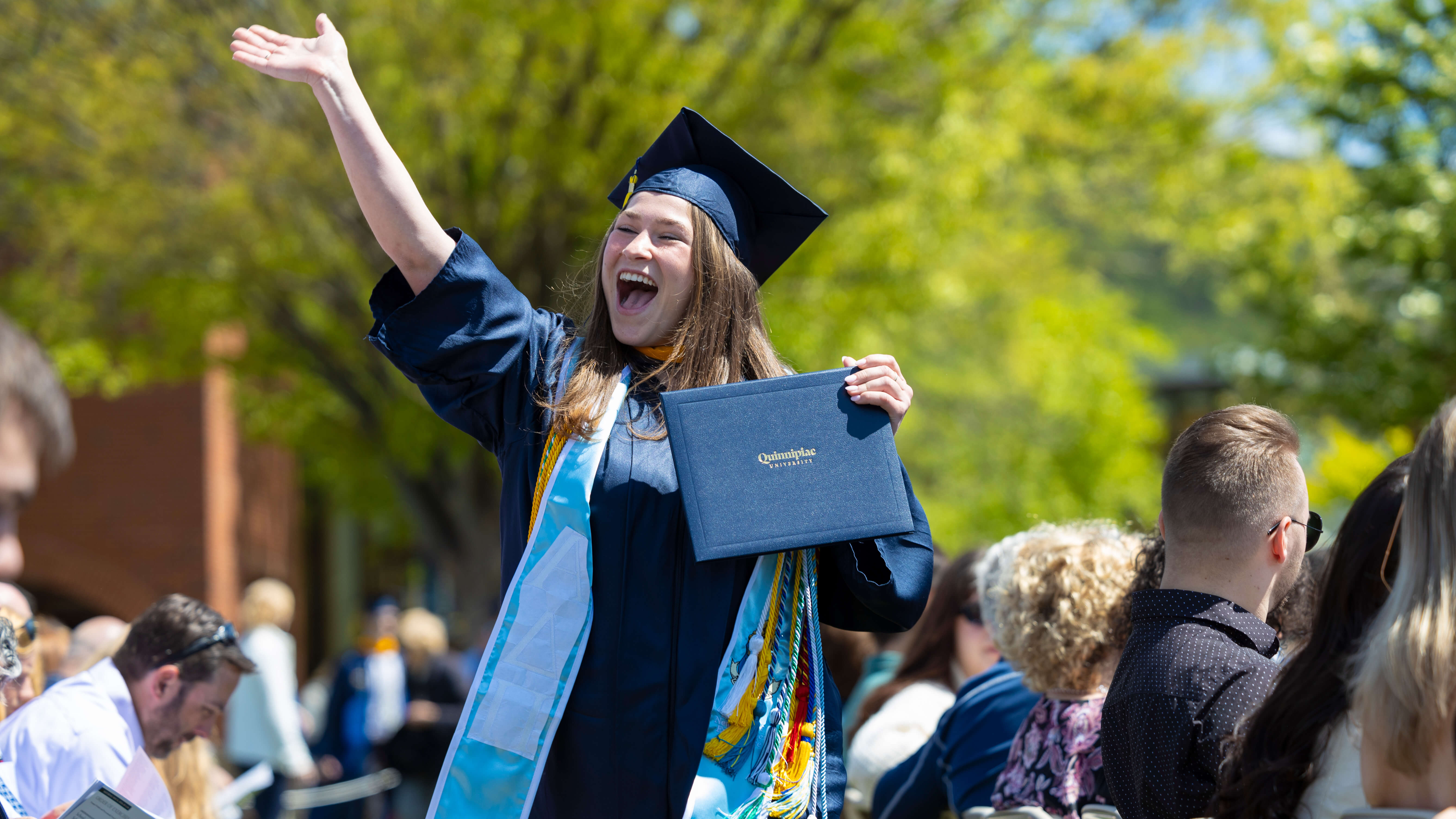 Student waves and smiles with degree