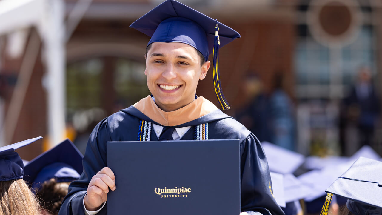 A graduate poses and smiles with his diploma