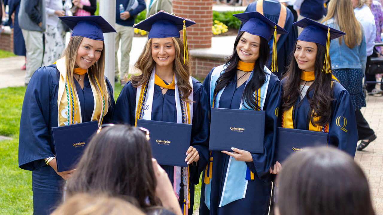 Four students smile in their navy and gold graduation caps and gowns