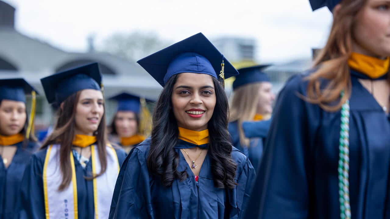 A graduate smiles to the camera as she walks