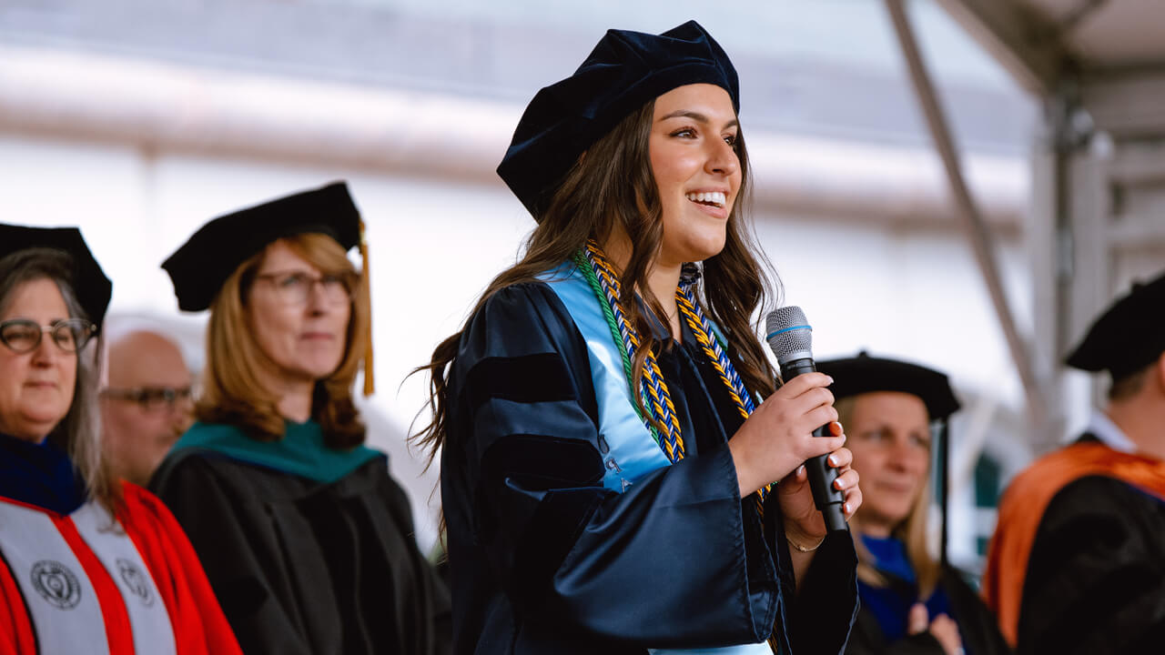 A graduate holds a microphone as she sings from the library steps