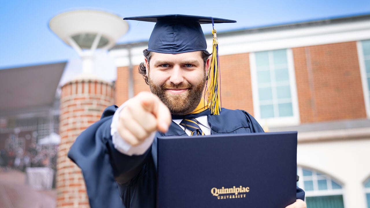 Student points at camera with degree