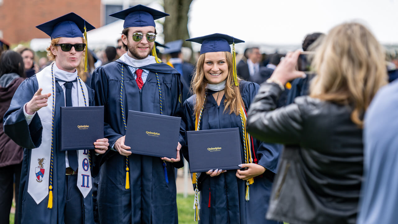 Three graduates pose with their diplomas as someone takes their photo