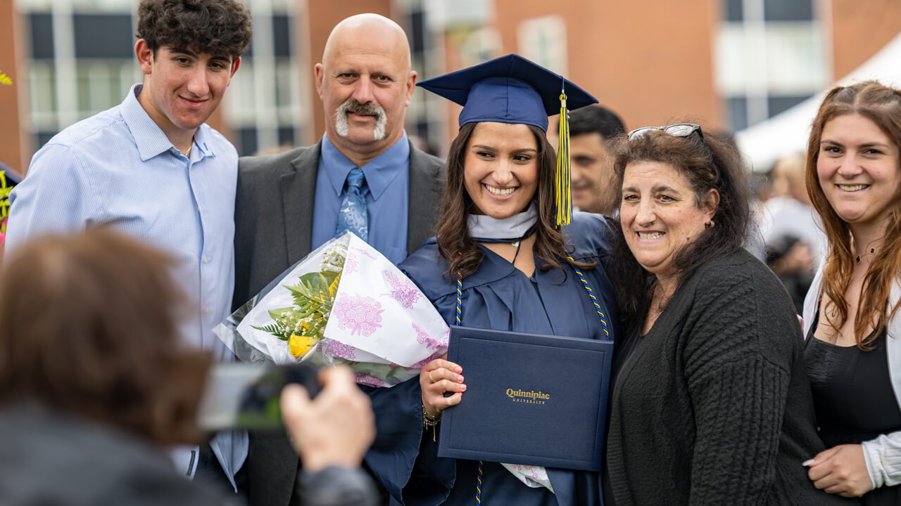 A graduate holding flowers and her diploma poses for a photo with her guests