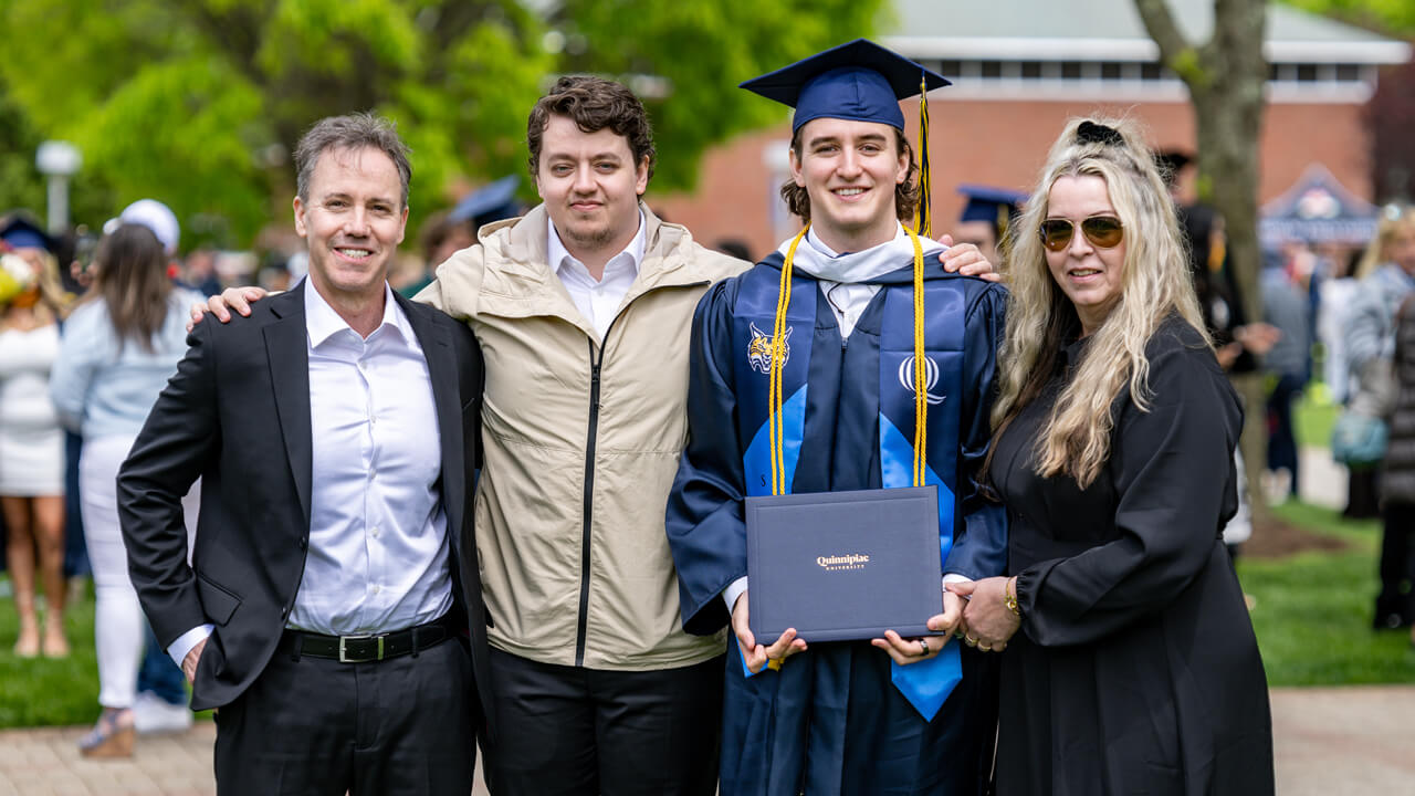 A graduate holds his diploma and poses for a photo with three of his guests