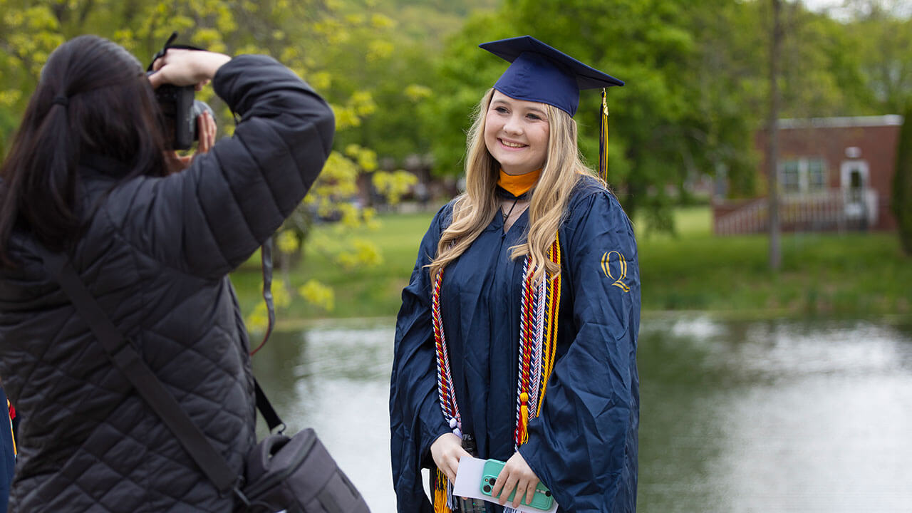 A graduate poses for a photo with her family member in front of a pond adjacent to the quad