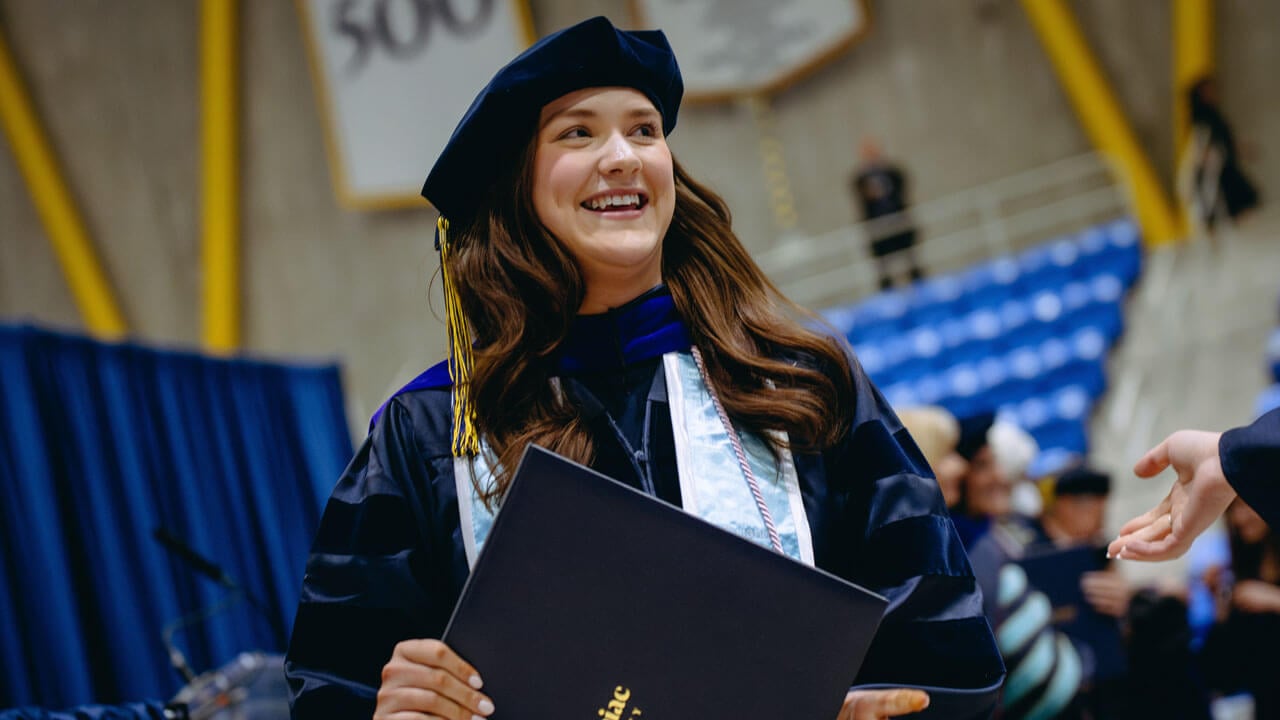 Law student smiling as she looks into the crowd holding her diploma