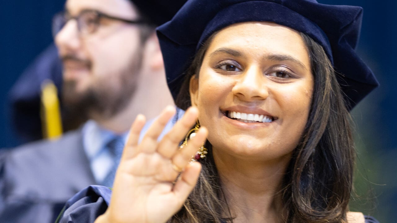 Medicine graduate smiling and waving at the camera with her cap