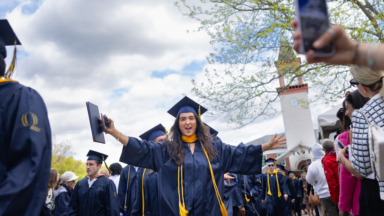 A graduate spreads her arms wide in celebration in front of the library clocktower