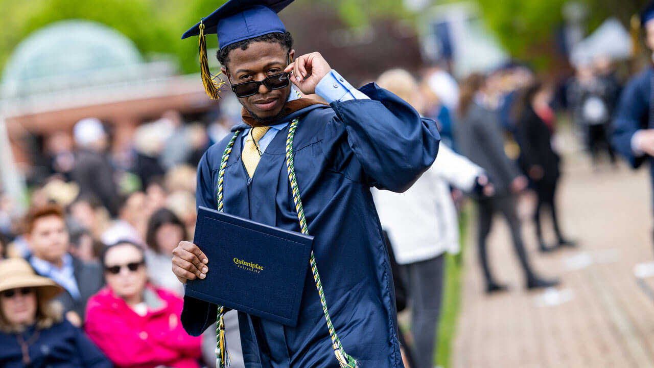 SOC graduate pulls down his glasses to look at the camera holding his degree