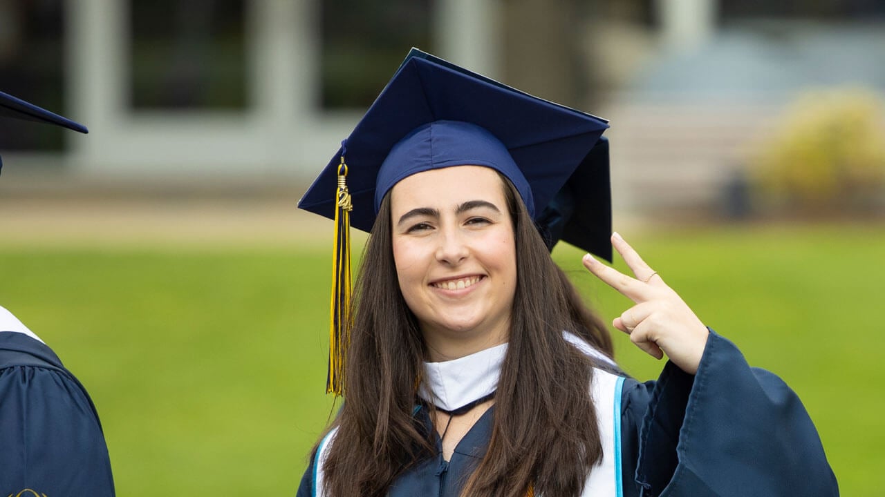 Graduate showing off peace sign and smiling during precession CAS Commencement