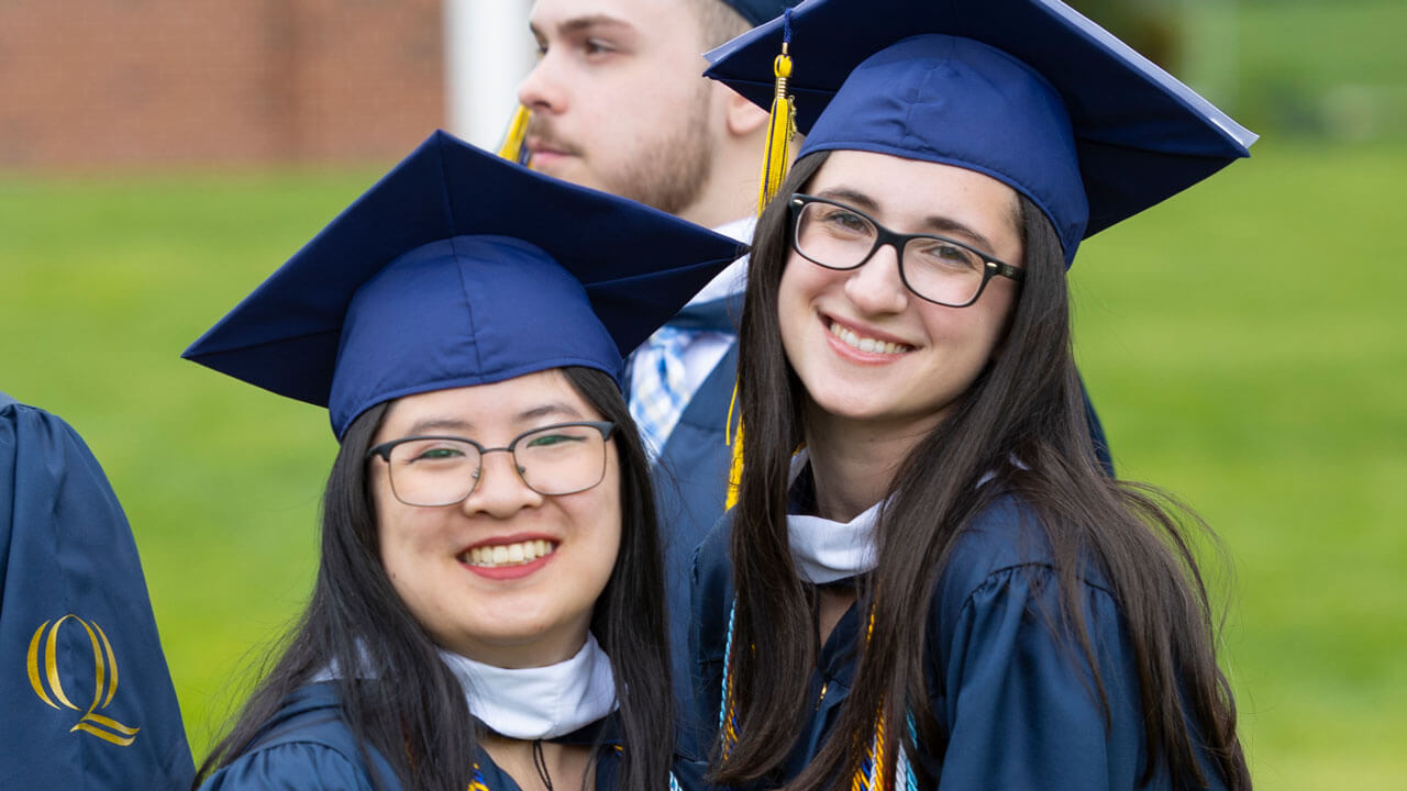 Two graduates smile and pose for a photo