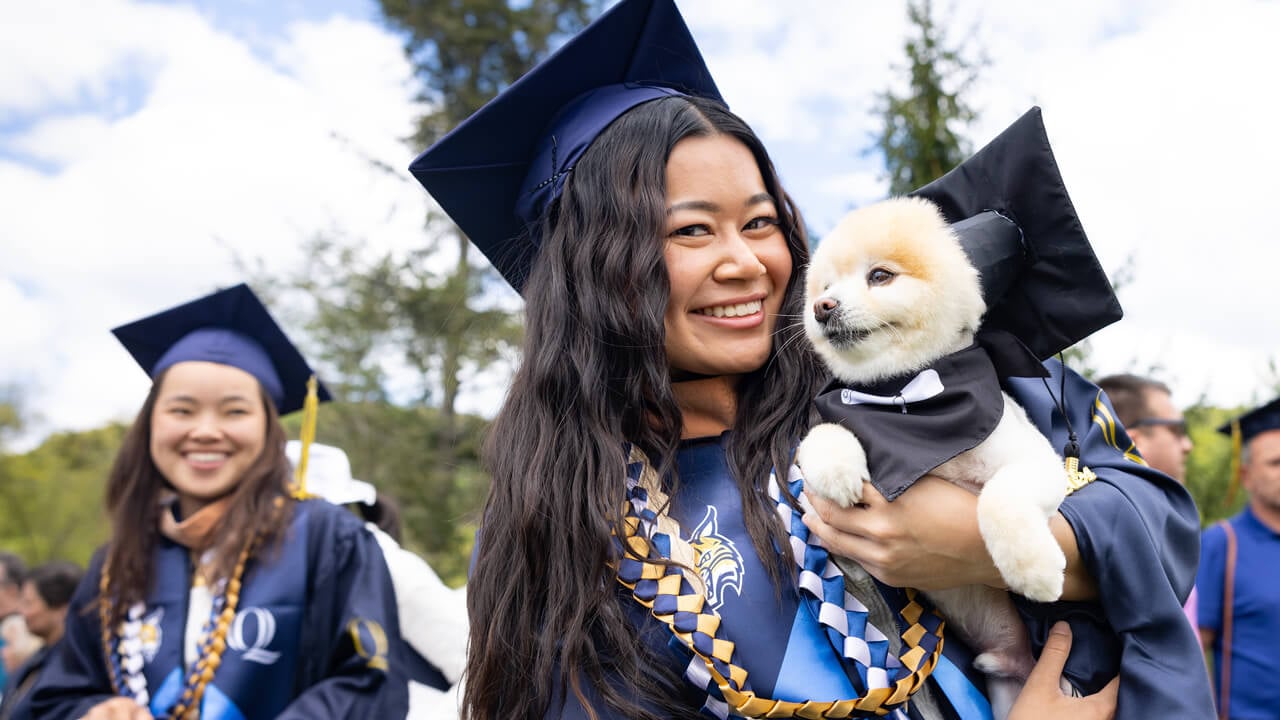 A graduate holds a small dog who is wearing a mini graduation cap