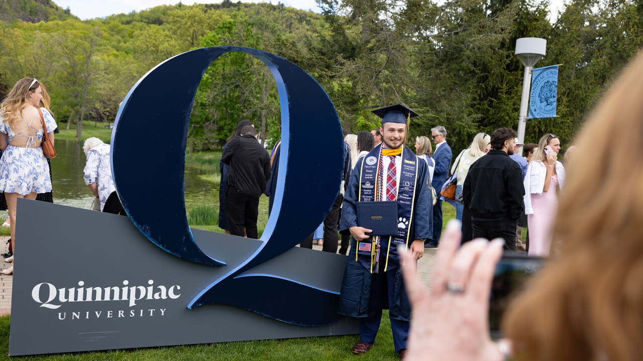 A graduate poses for a photo in front of a giant Quinnipiac Q sign