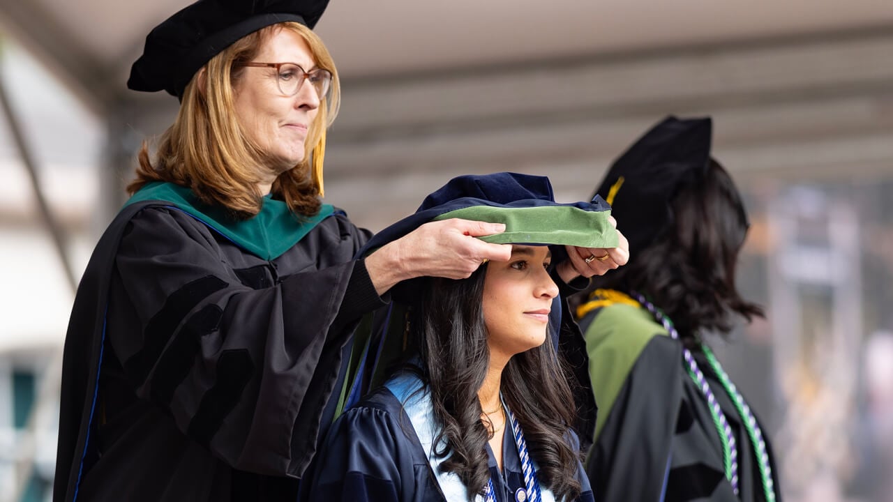 A faculty member places a doctoral hood over the head of a new graduate