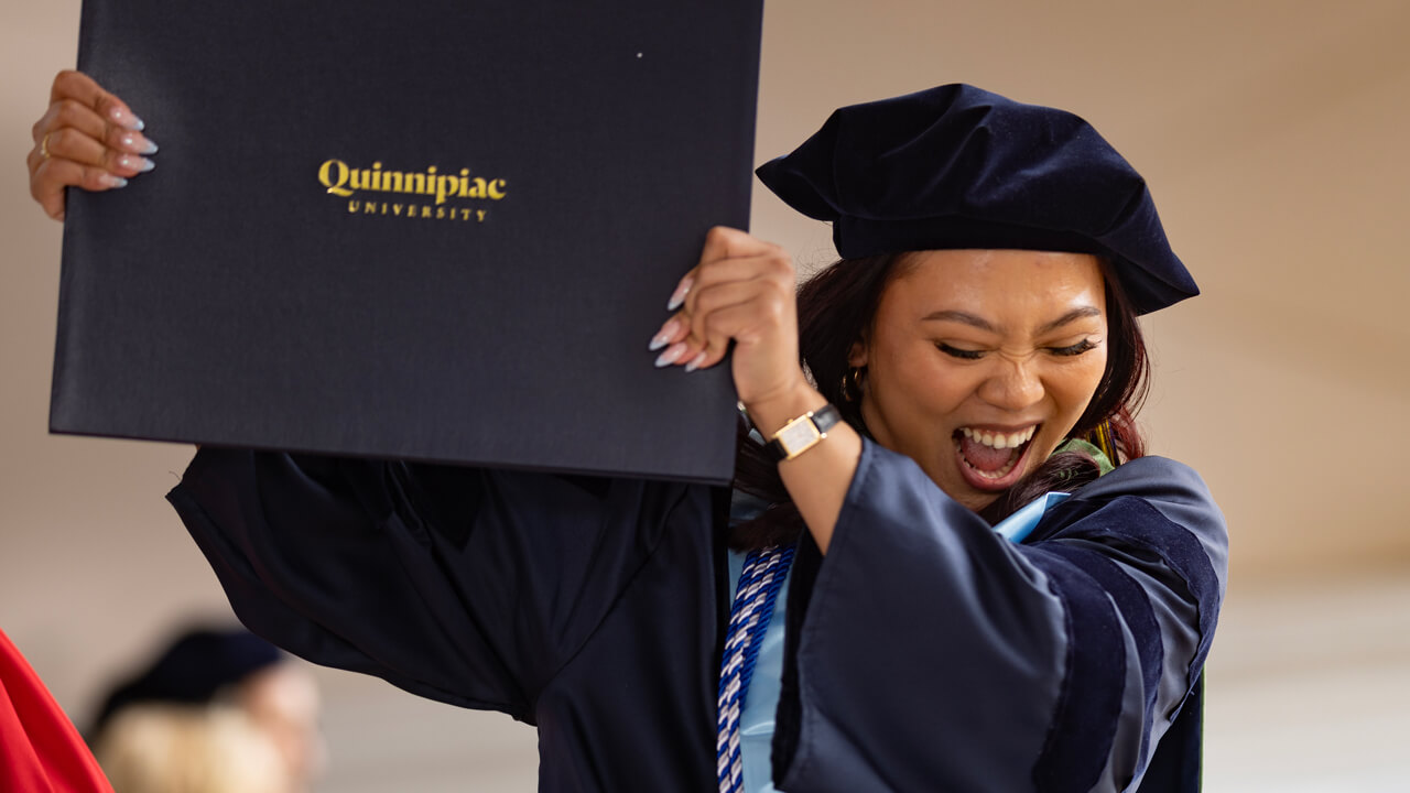 A graduate cheers enthusiastically as she holds her diploma up over her head