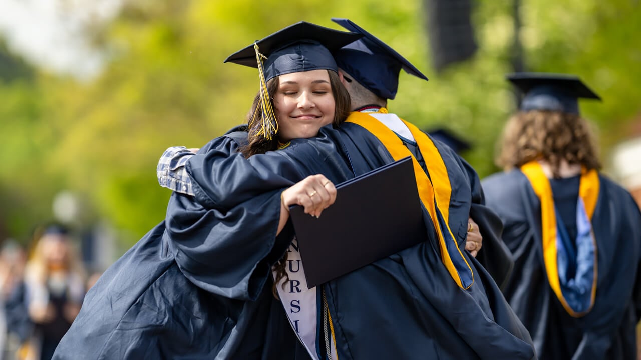 Two graduates smile as they warmly hug