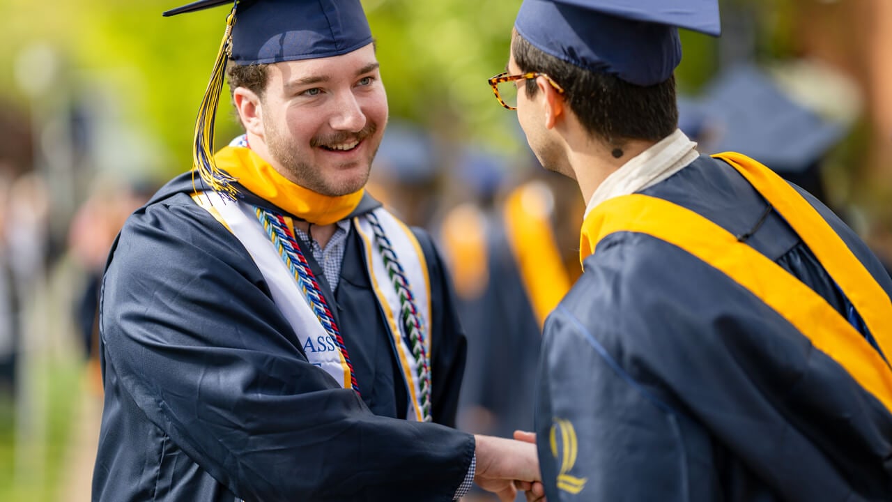 Two graduates shake hands in congratulations
