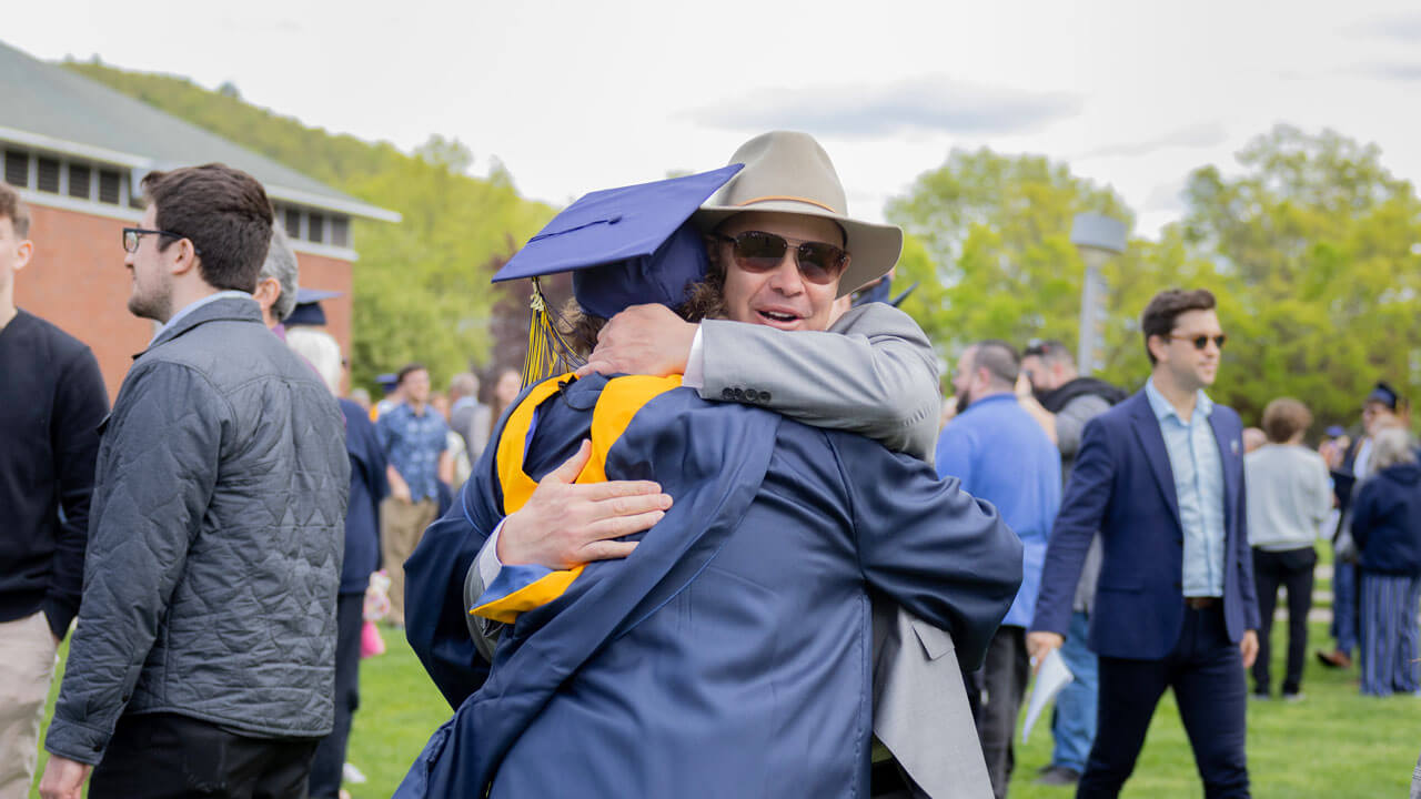 Father hugs a graduate in a navy and gold cap and gown