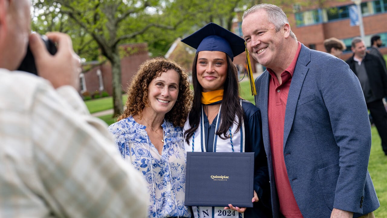 A graduate holds her diploma and poses with her parents for a photo
