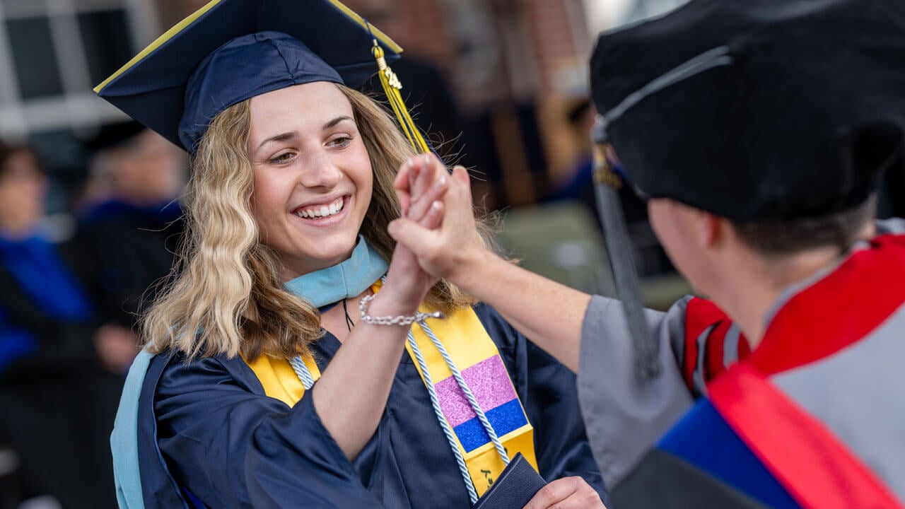 Quinnipiac graduate grabs their friends hand smiling