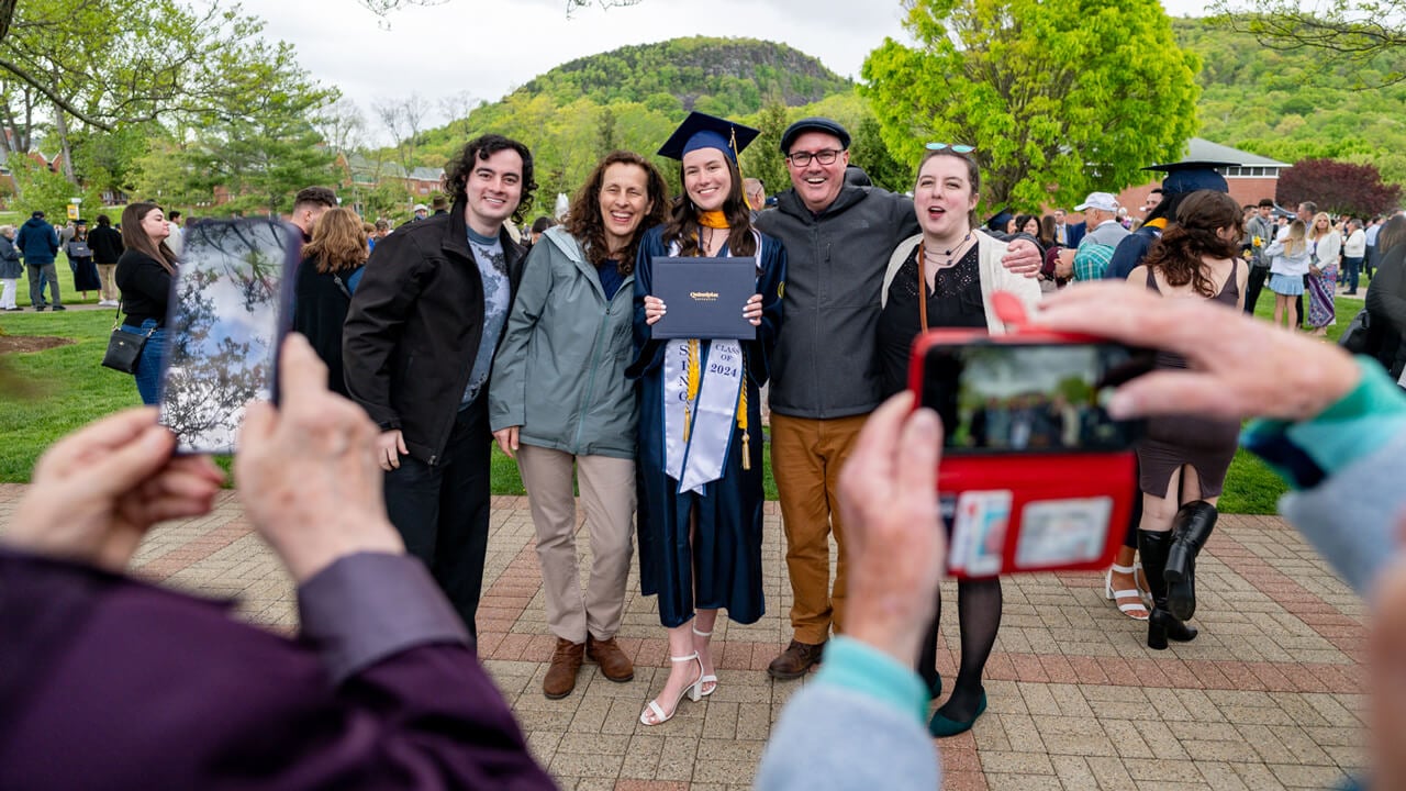 A graduate and her guests pose while two people take their photo