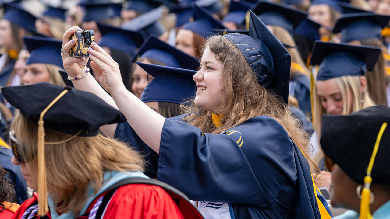 Quinnipiac graduate standing out of her seat taking a photo with her phone