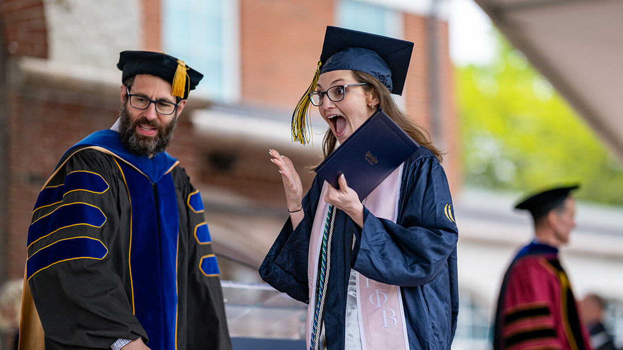 graduate shares excited expression while holding diploma
