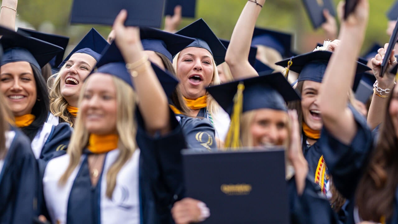 graduates applaud and raise their diplomas