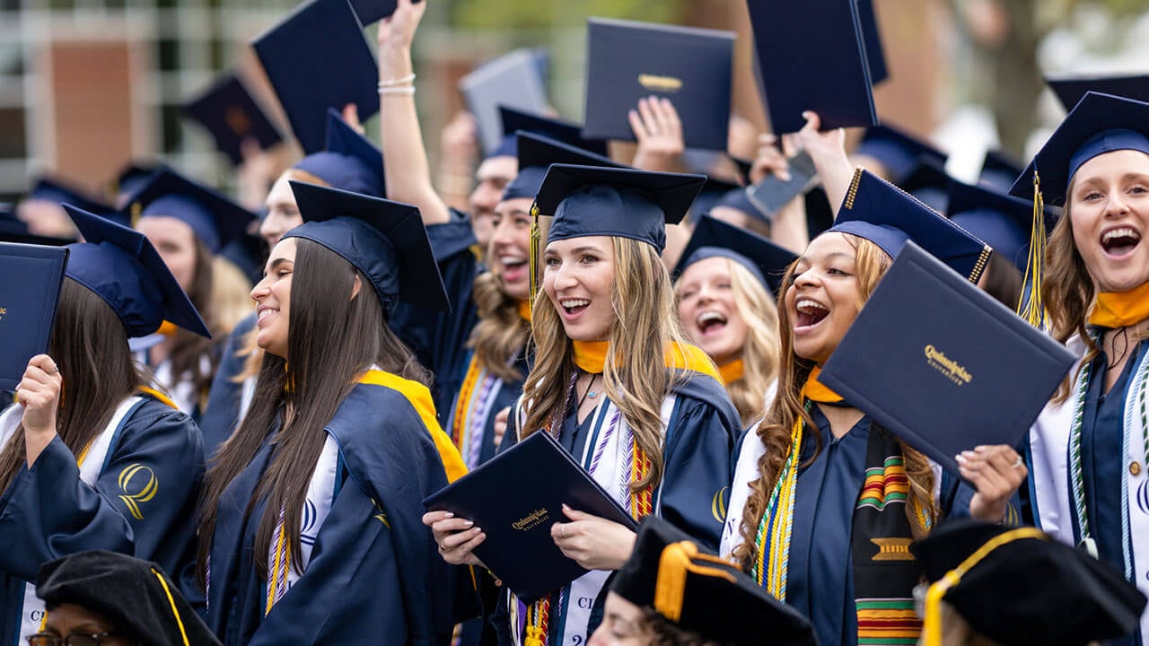 graduates cheer and raise their diplomas