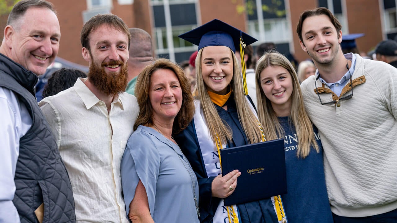 Quinnipiac graduate posing for a photo with their family and holds up their diploma