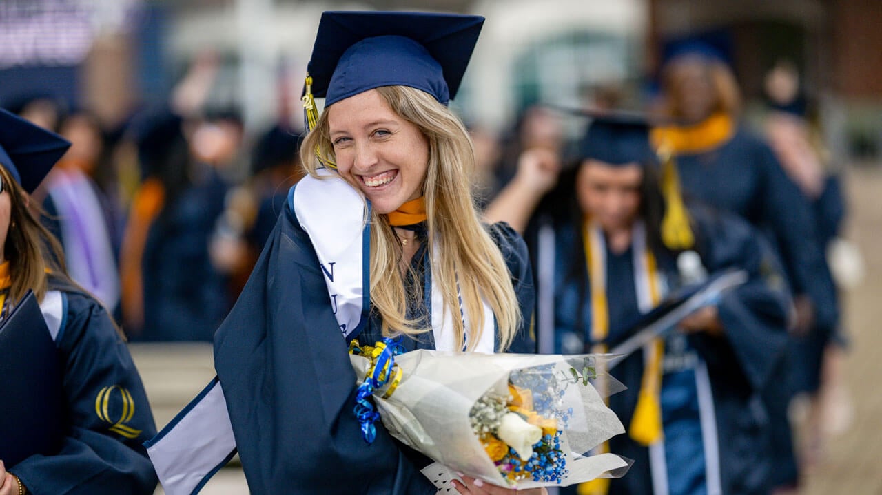 Graduate smiles while holding their blue and yellow flowers