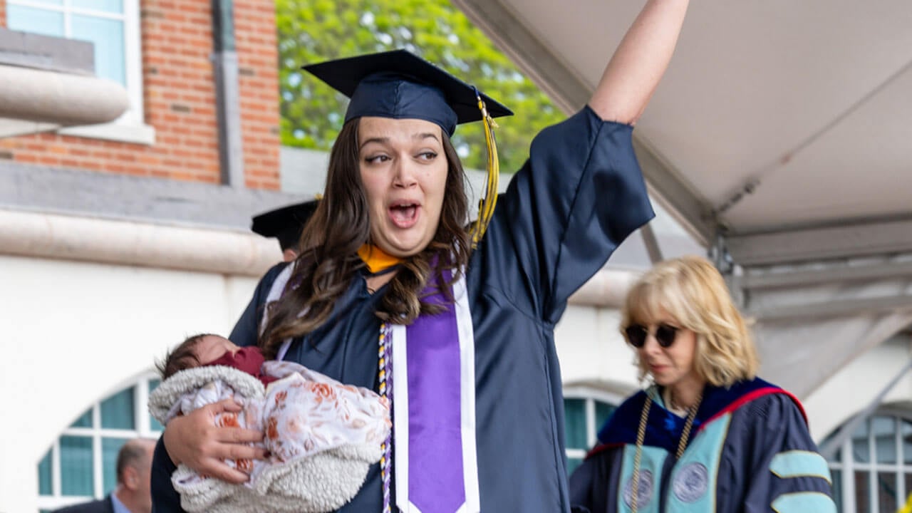 graduate waves from the stage while holding a baby