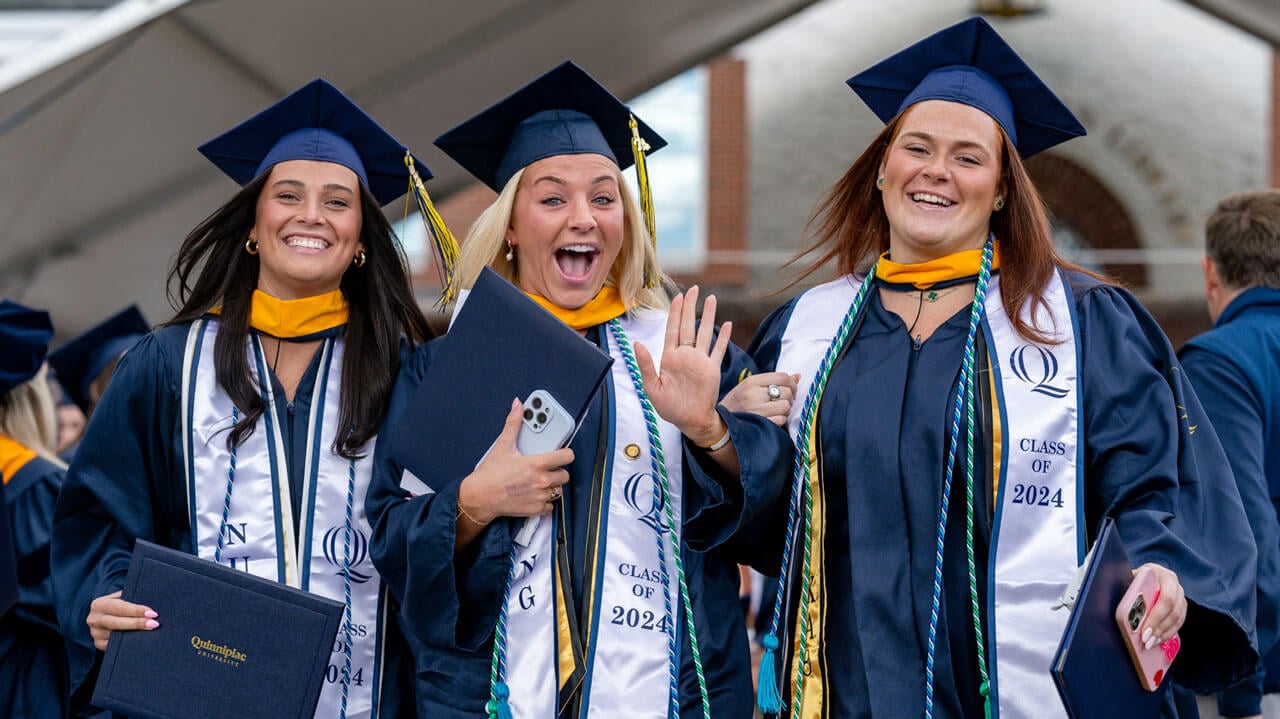 Three School of Nursing graduates beam and wave at the camera after being given their diplomas.