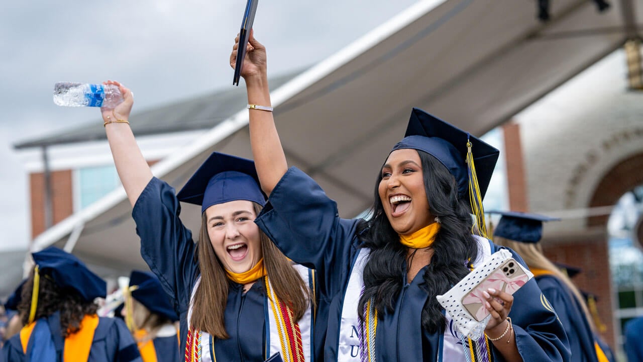 Two 2024 School of Nursing graduates rejoice during the Commencement ceremony as they raise their arms in celebration.