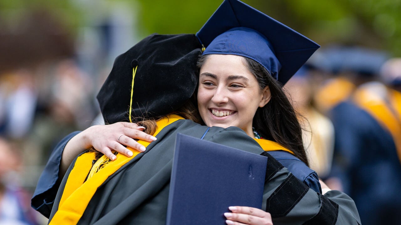 Graduate hugging their friend with their degree in hand