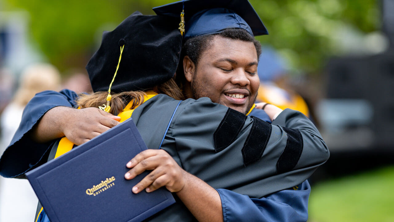 Graduate hugging their professor holding their degree