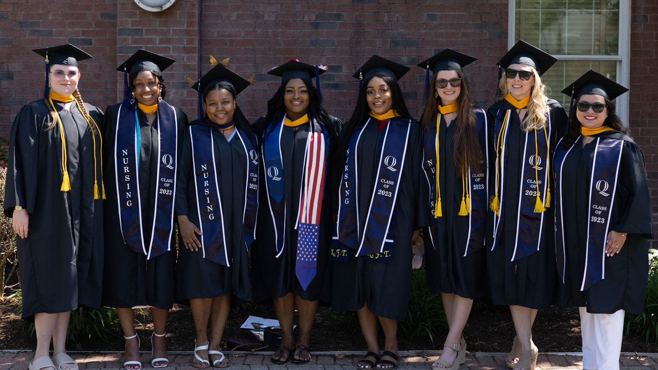 Eight graduates with navy Class of 2023 stoles pose for a photo arm in arm